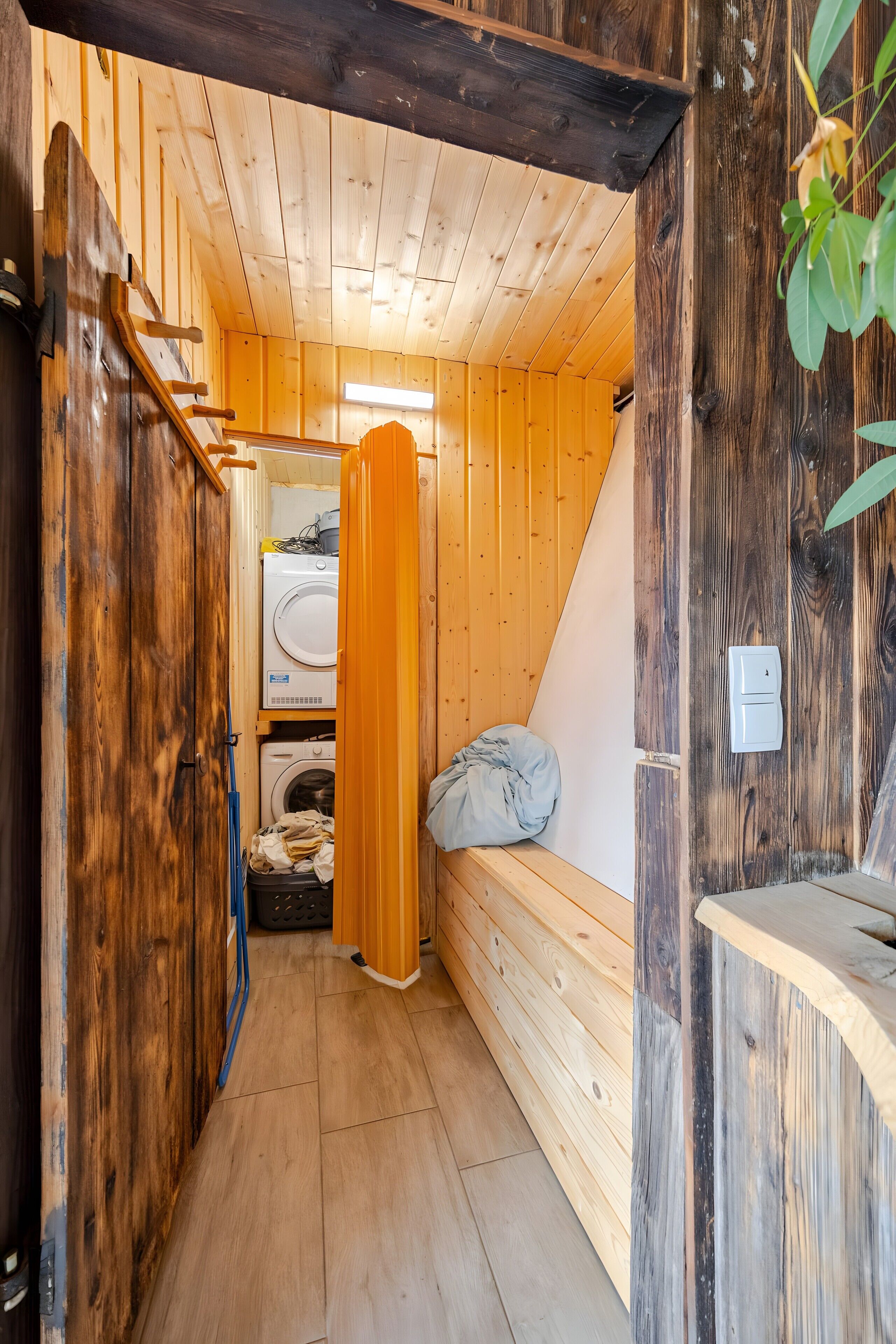 A narrow wooden hallway with a bench, a washing machine, and a bed.