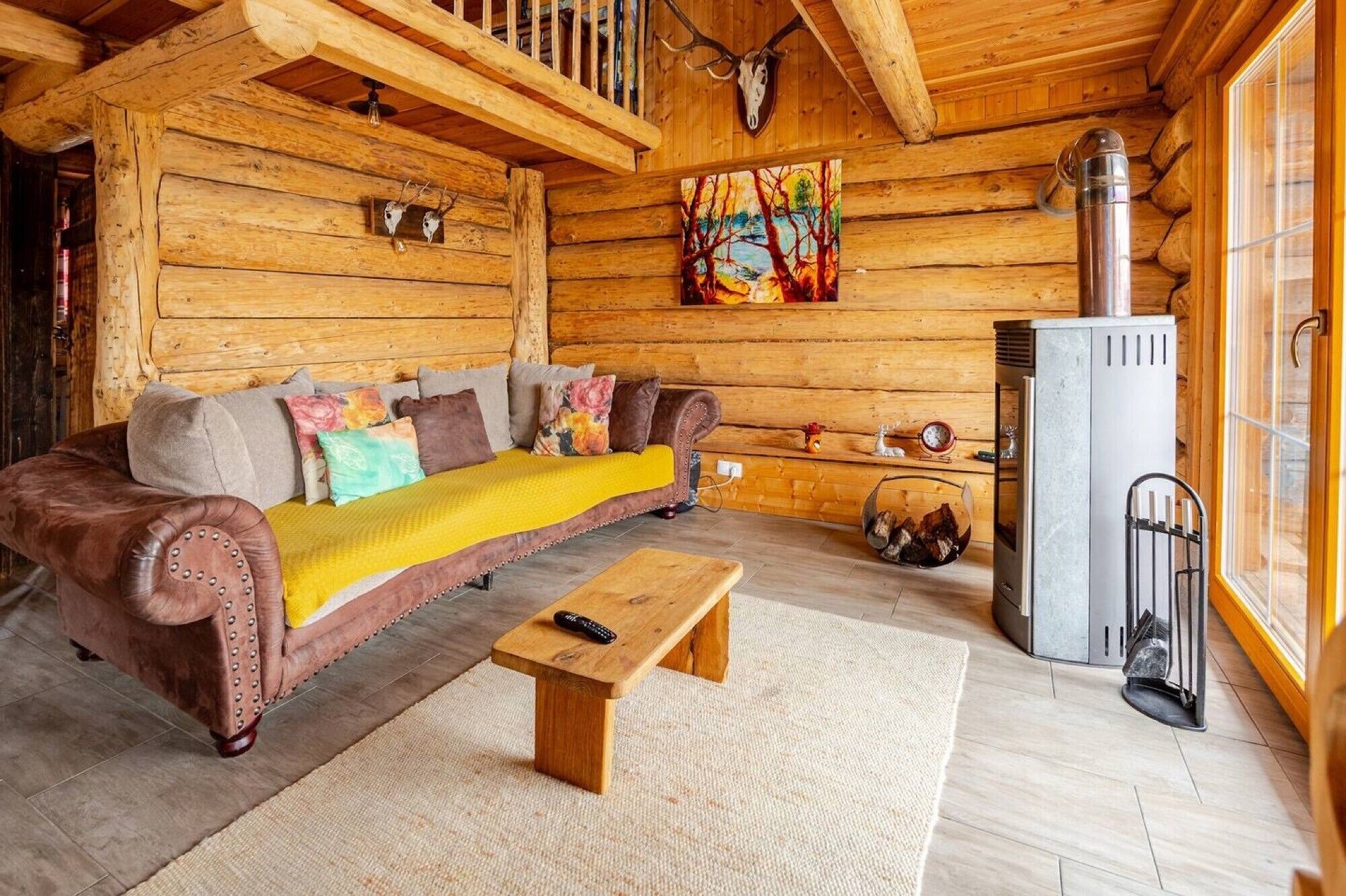 En mysig stuga med träpanel på väggarna, en soffa i trä, ett litet träbord, en öppen spis och en tavla på väggen.