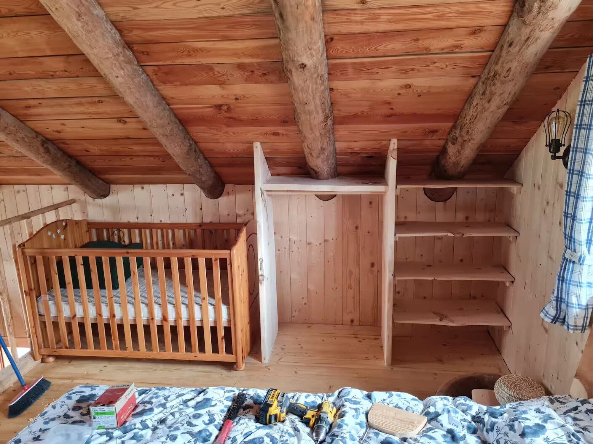 A wooden cabin interior with a crib, shelves, and a bed with a floral-patterned blanket.