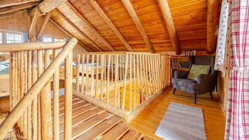 A wooden interior with a balcony, a chair, and a bookshelf.