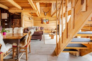 A wooden interior with a dining table, chairs, a sofa, and a staircase.