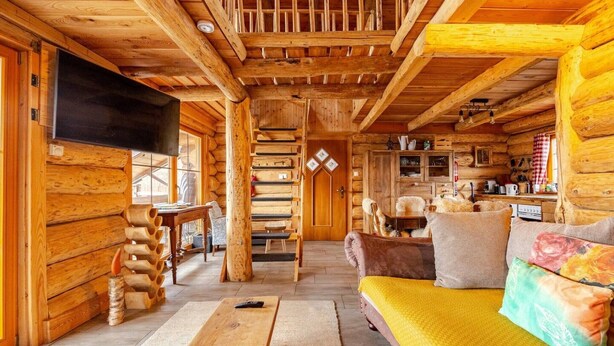 Interior de uma cabana de tronco com um banco de madeira, sofá e área de jantar.