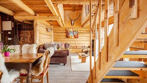 Interior rústico de uma cabana com uma mesa de jantar de madeira, um sofá e uma lareira.