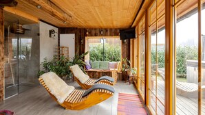Interior em madeira com duas cadeiras estofadas, chuveiro de vidro e vista para o verde lá fora.