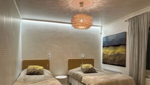 Quarto com duas camas, luminária pendente, radiador e um quadro na parede.