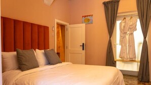 Habitación de hotel con cama, puerta, ventana con cortinas y un cuadro en la pared.