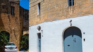 Una calle estrecha con un edificio blanco que tiene una puerta y ventana azules, junto a un edificio de piedra.