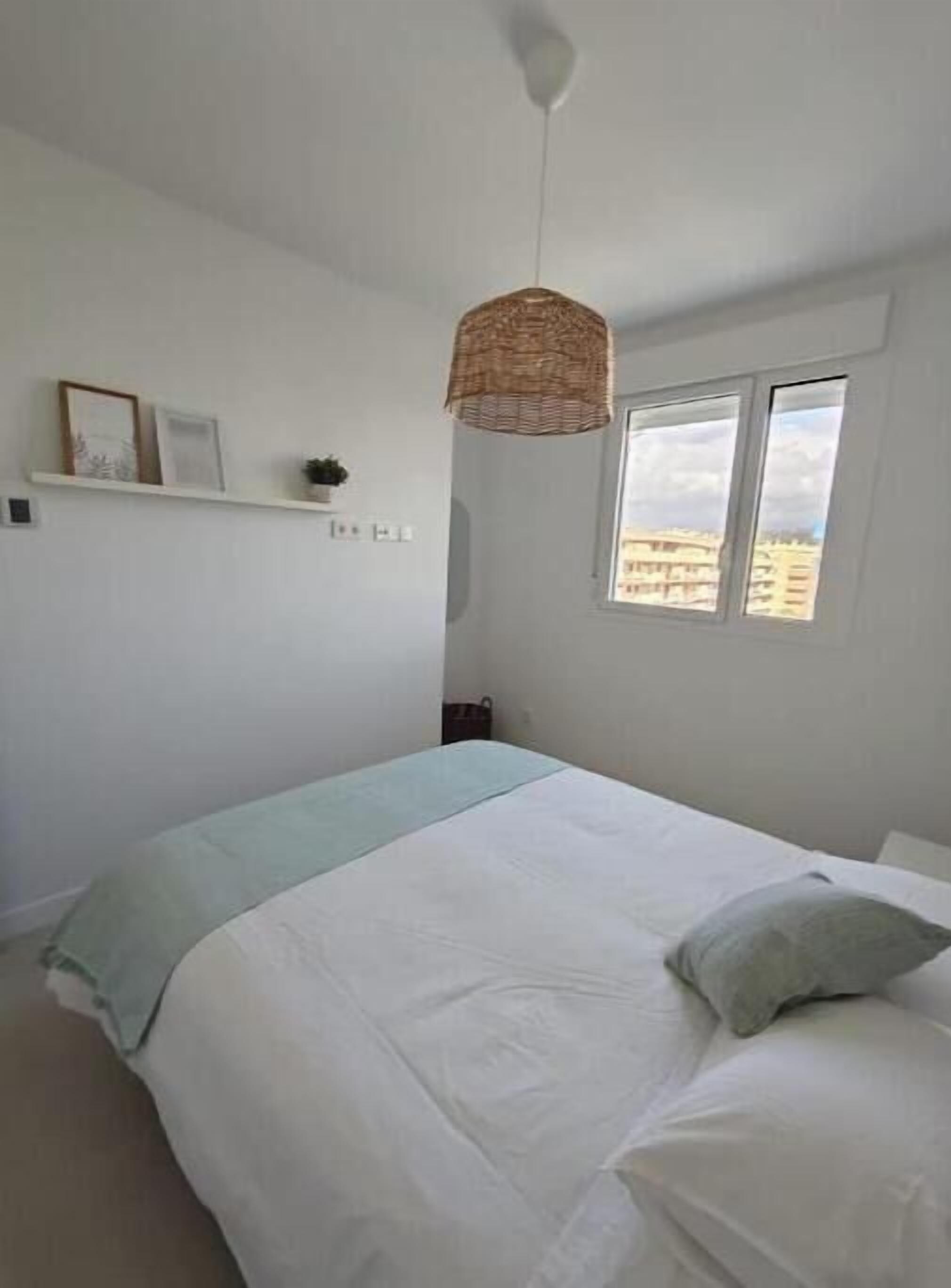 Een slaapkamer met een bed, een hanglamp, een raam en een plank met spullen.