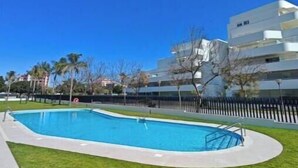 A swimming pool with a clear blue sky, surrounded by a grassy area and a modern building in the background. - New apartment near the beach - medium term stays (ideal for couples) (Torre del Mar)
