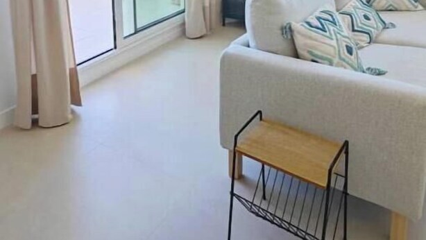 A modern living room with a sofa, a small wooden bench, and a view of buildings through large windows. - New apartment near the beach - medium term stays (ideal for couples) (Torre del Mar)