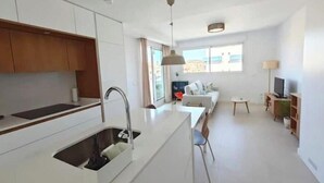 A modern kitchen with a built-in sink, a dining area with a table and chairs, a sofa, and a TV. - New apartment near the beach - medium term stays (ideal for couples) (Torre del Mar)