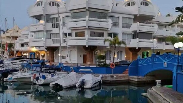 Ein Hotel am Wasser mit mehreren Balkonen, einem spiegelnden Pool und anlegenden Booten.