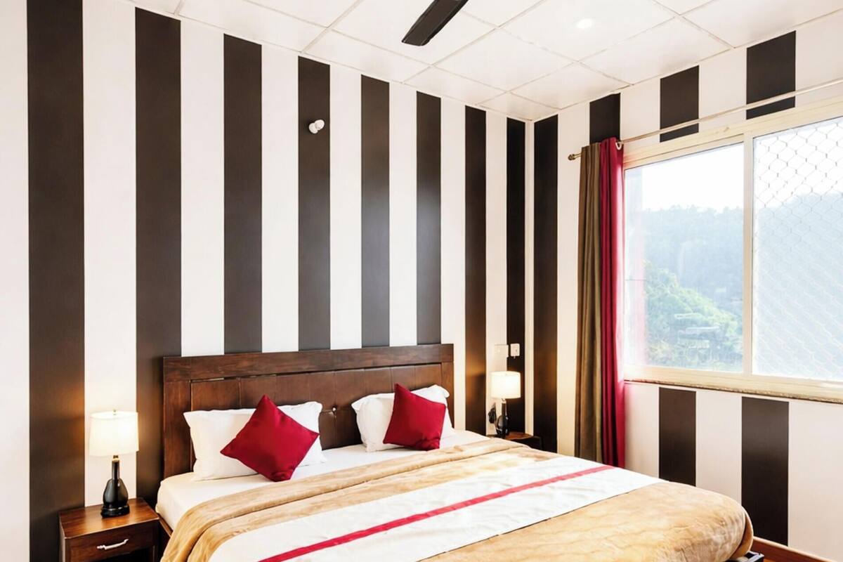 Un dormitorio con una cama de madera, un ventilador de techo, una mesita de noche y un ventanal con cortinas.