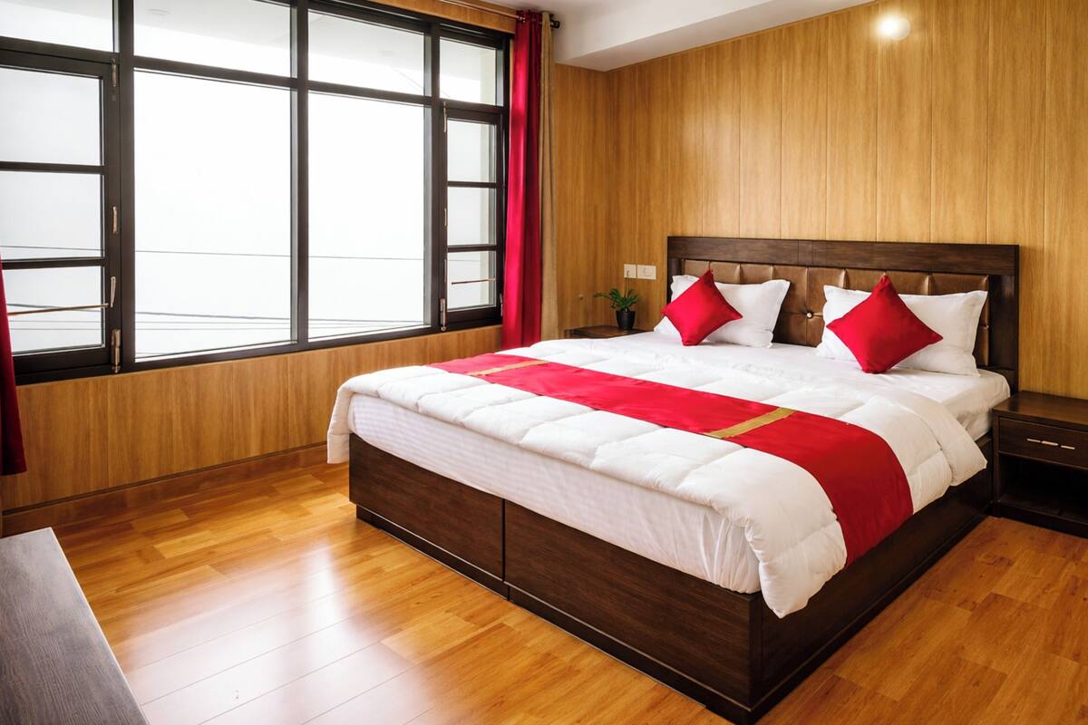 Habitación de hotel con una cama grande, paredes de madera, una ventana con cortinas y una mesita de noche.
