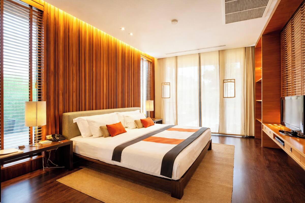 Una habitación de hotel moderna con una cama grande, paneles de madera, un televisor y vistas al exterior.