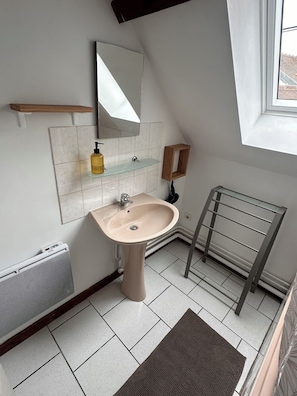 A bathroom with a pedestal sink, a mirror, a towel rack, a shelf with a bottle, and a radiator.