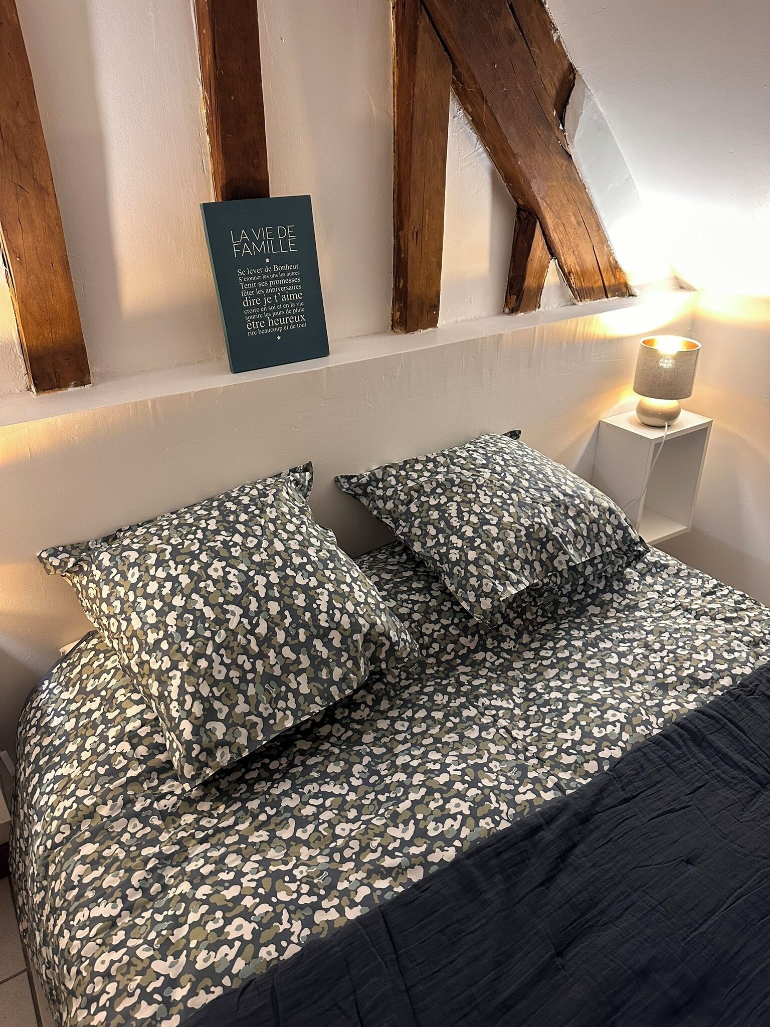 Une chambre à coucher avec un lit, deux oreillers, une lampe de chevet et une citation inspirante sur le mur.