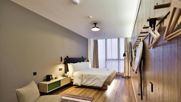Een hotelkamer met een bed, een stoel, een nachtkastje, een lamp, een kledingkast en een raam met gordijnen.