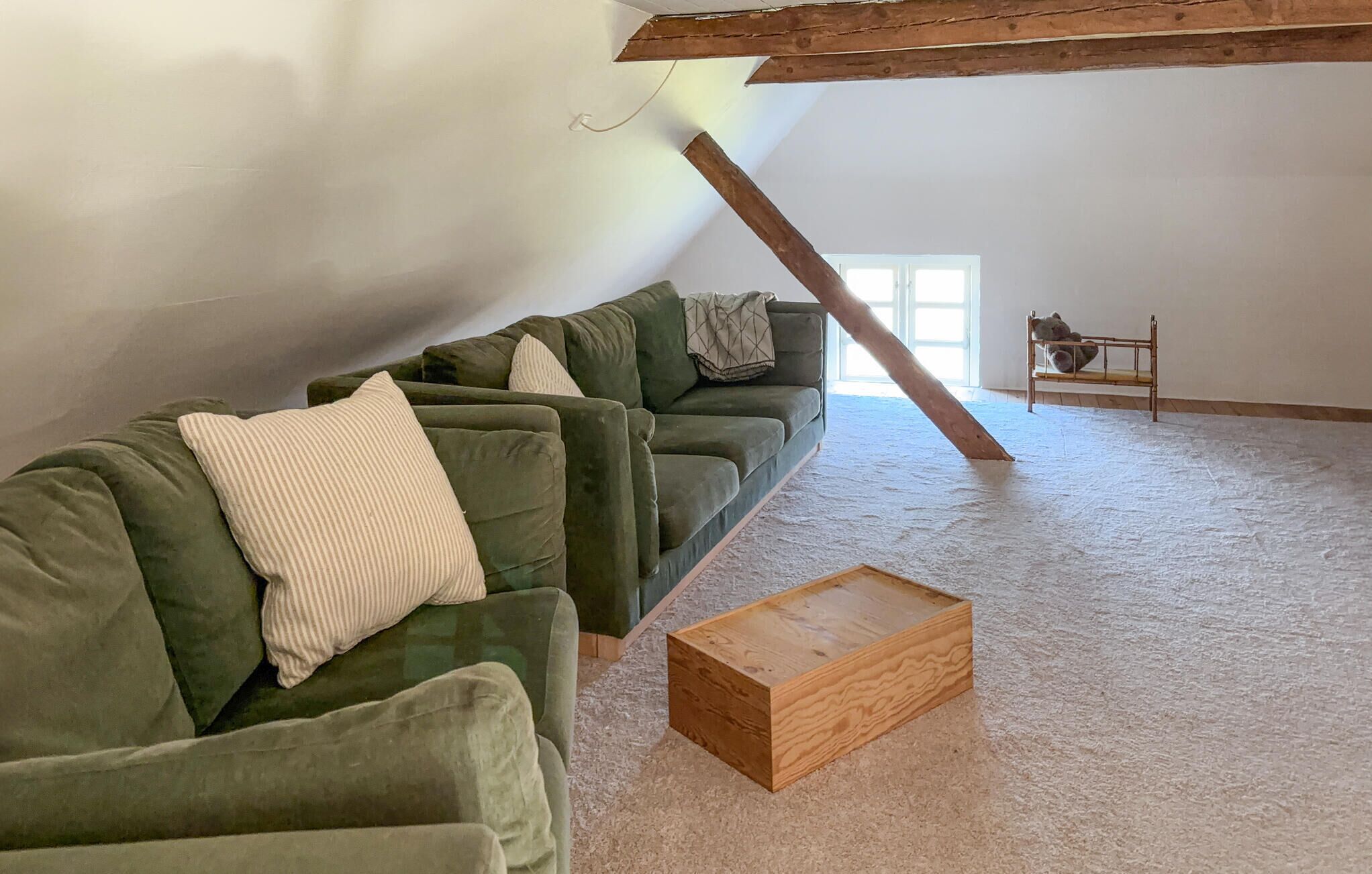 A loft-style room with a green sectional sofa, a wooden coffee table, and a small bench with a teddy bear.