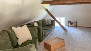 Un espacio tipo loft con un sofá seccional verde, una mesa de centro de madera y un pequeño banco con un osito de peluche.