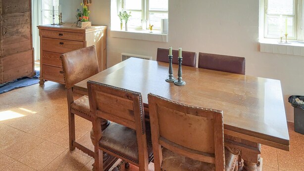 Una mesa de madera con cuatro sillas, un armario de madera y una ventana con cortinas.