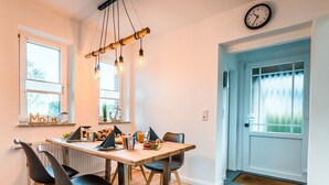 Un coin repas avec une table en bois, des chaises noires, un luminaire suspendu et une horloge au mur.