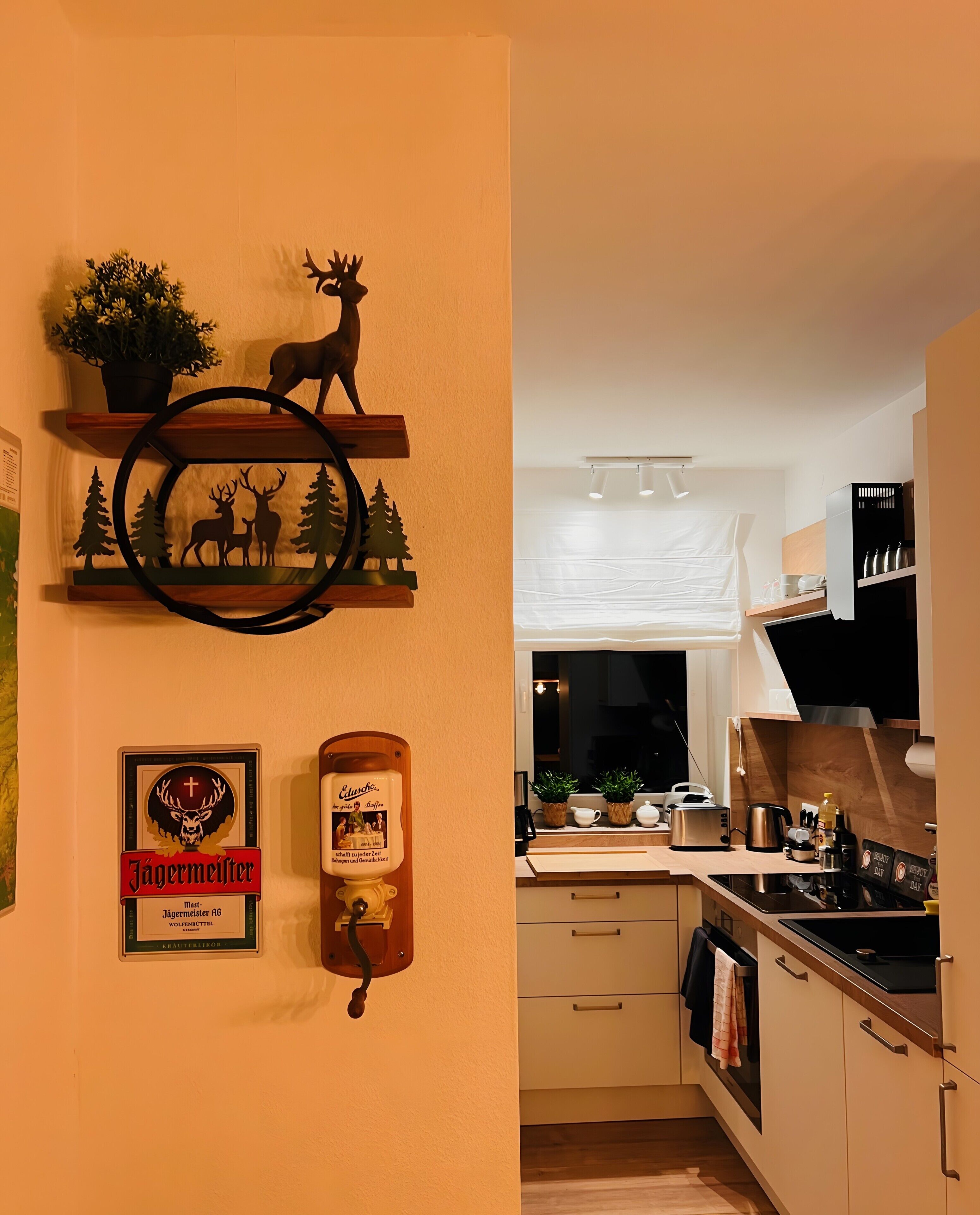 A kitchen with wooden shelves, a deer's silhouette, a beer tap, and a window with a view.