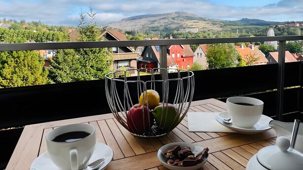 Een balkon met een tafeltje gedekt voor twee personen, inclusief een kop koffie, een schaal fruit en een schaal chocolade.