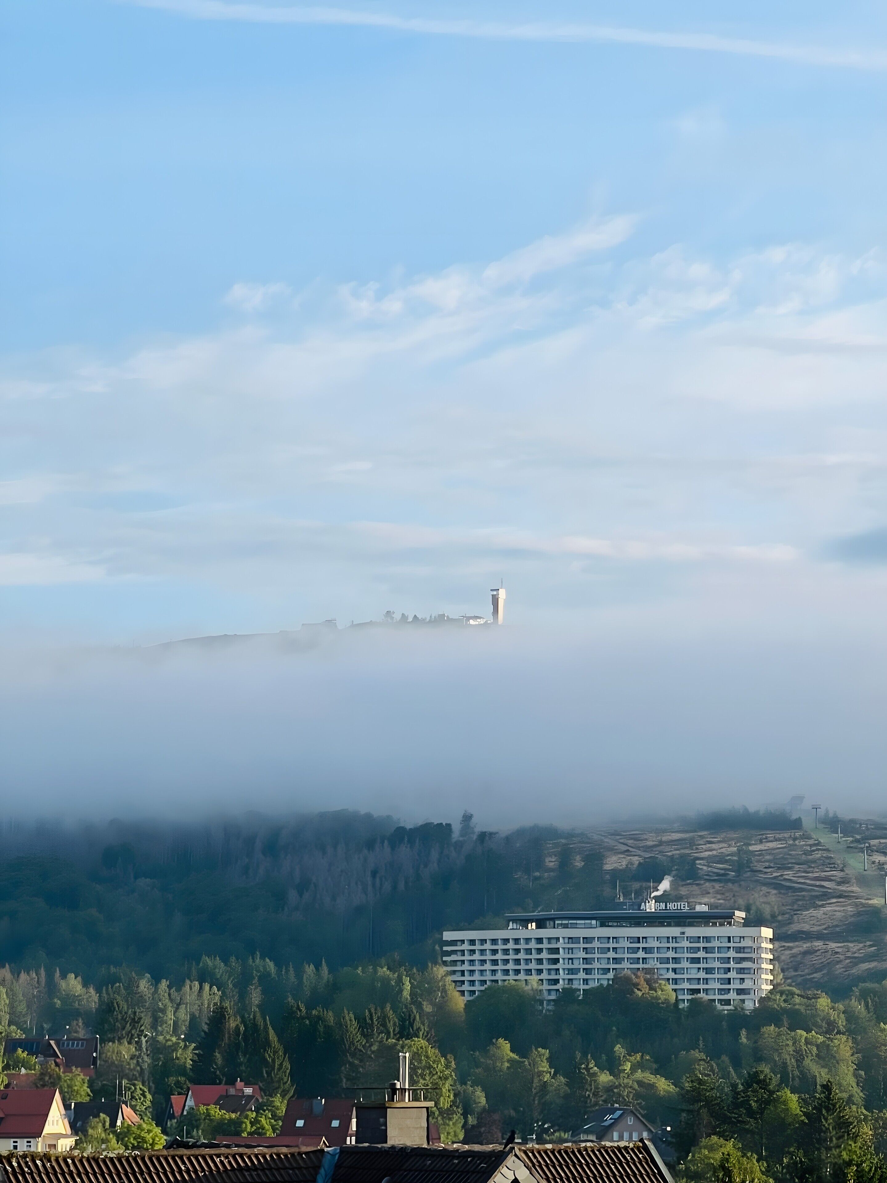 A hotel with a flat roof, surrounded by trees and a foggy landscape.