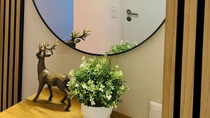 Een ronde spiegel aan een muur met een deur, ingelijste foto's en een decoratief hert en plant.