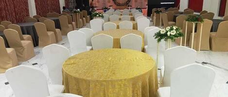 A banquet hall with round tables, white chairs, and a stage with a screen.