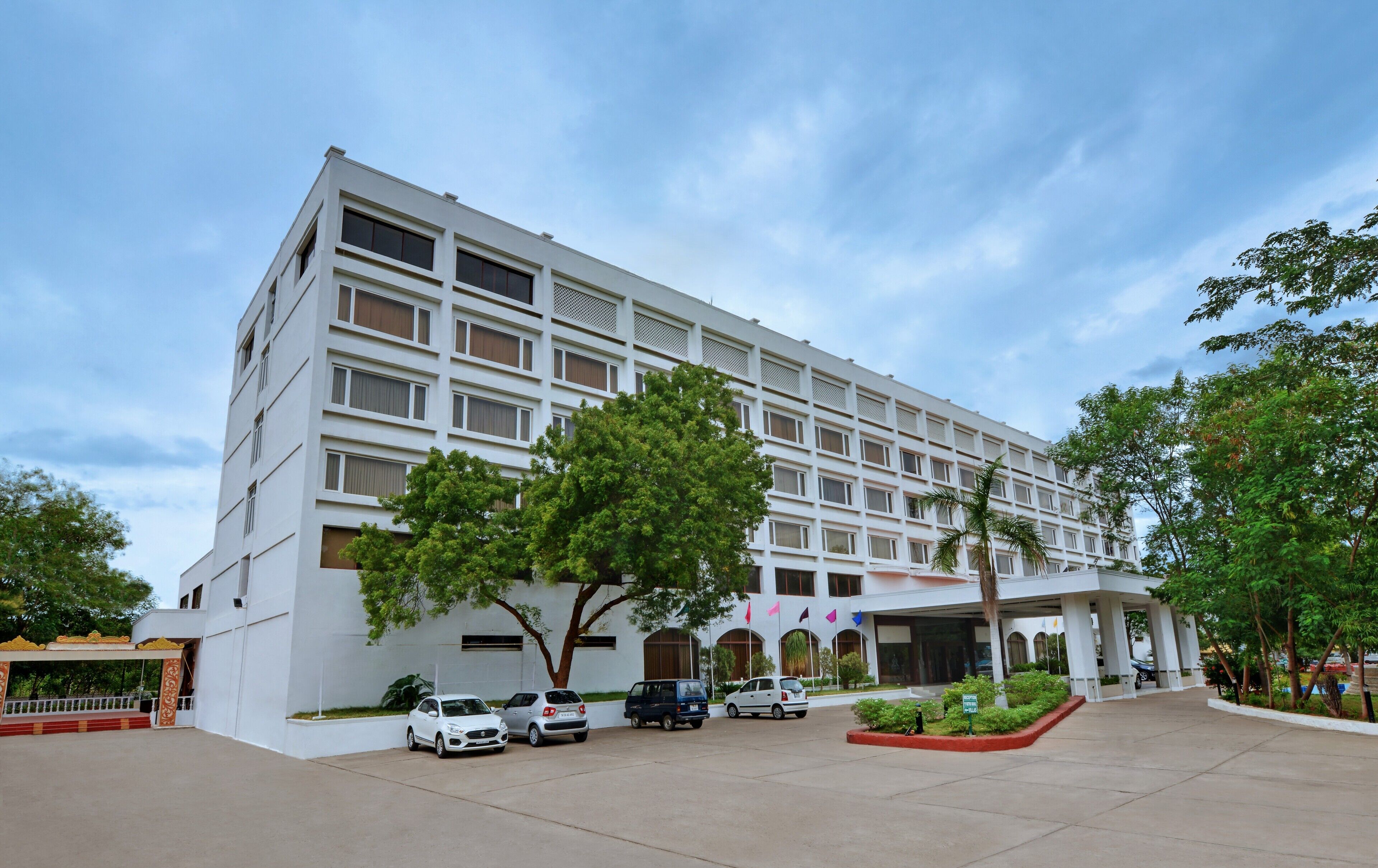 A multi-story building with a flat facade, large windows, and a covered entrance area with a few cars parked in front.