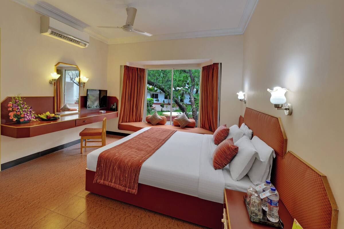 Une chambre d’hôtel avec un lit, un bureau et une chaise, un miroir et une fenêtre avec des rideaux.