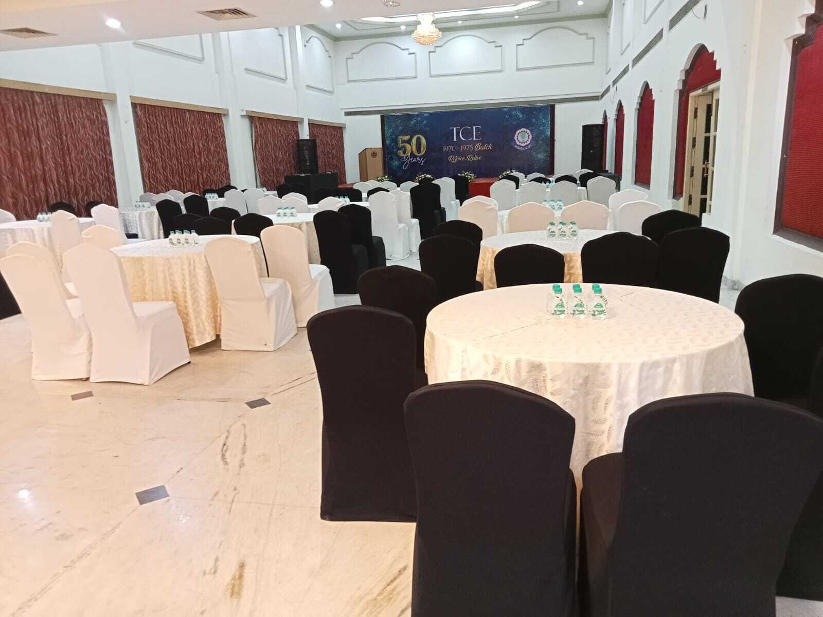 A banquet hall with round tables, chairs, and a stage with a banner.