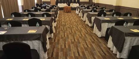 Un salón de conferencias con filas de mesas, sillas y un atril al frente.
