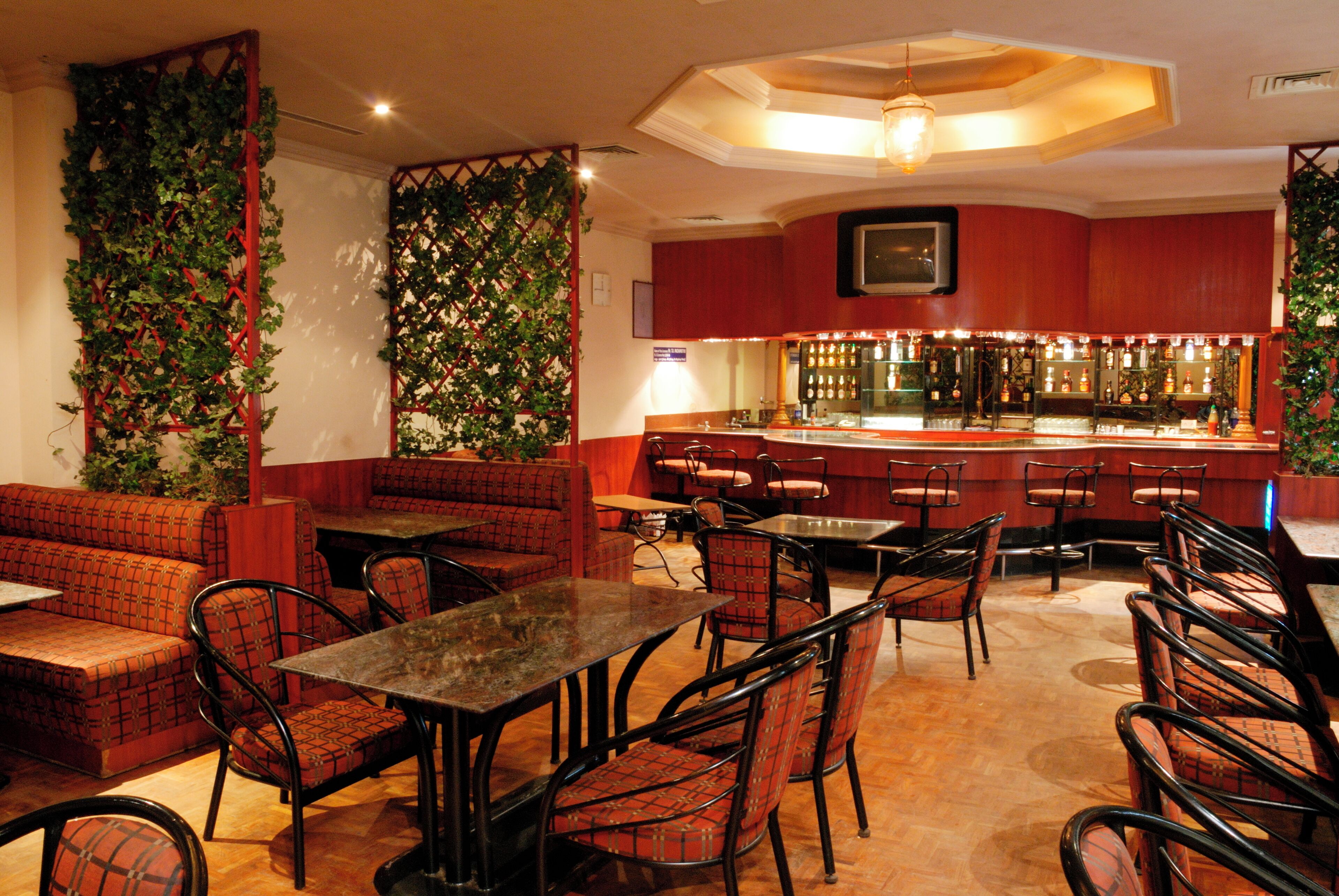 A restaurant with booths, tables, and chairs, a bar area, and decorative greenery.