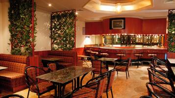 A restaurant with booths, tables, and chairs, a bar area, and decorative greenery.