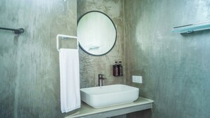 Ein Badezimmer mit einem weißen Waschbecken, einem runden Spiegel, einem Handtuch auf einem Wäscheständer und zwei Shampoo-Flaschen.