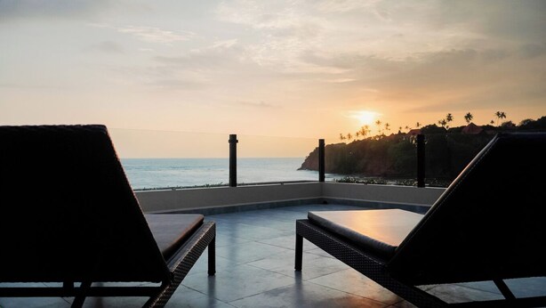 Eine Terrasse mit zwei Liegestühlen und Blick auf das Meer bei Sonnenuntergang.
