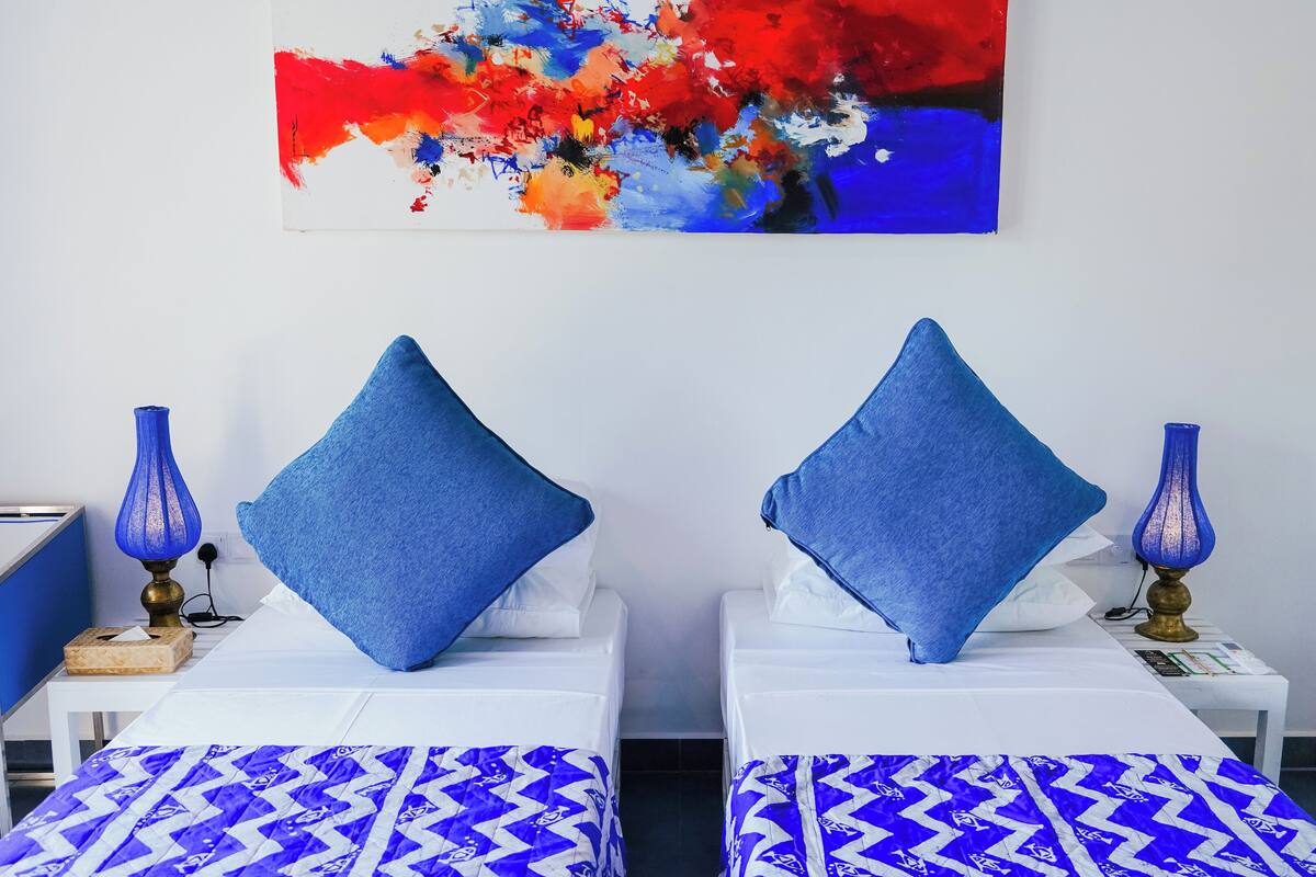Une chambre d’hôtel avec deux lits, chacun agrémenté d’un oreiller bleu et d’une couvre-lit à motifs.
