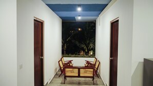 Ein Korridor mit Tisch und Stühlen, einer Deckenleuchte und Blick auf einen Garten bei Nacht.