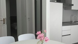 Una cucina moderna con mobili bianchi, un forno a microonde e un lavello. C'è un tavolo da pranzo bianco con un vaso di fiori rosa.