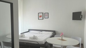 Una camera d'albergo con un letto, un tavolo rotondo con sedie, un tavolino con un vaso e due quadri appesi al muro.