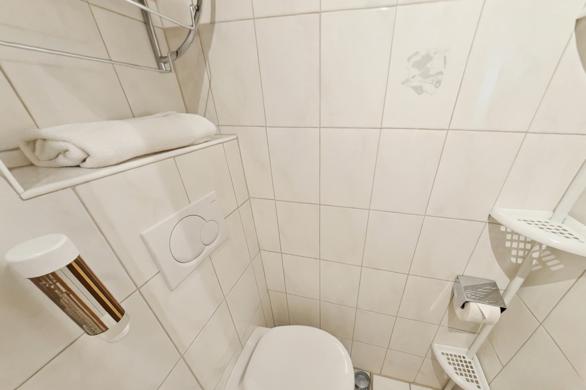 A small, clean bathroom with a toilet, a towel rack, a soap dispenser, and a shower area.