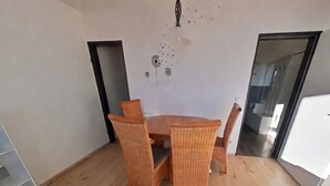 Ein Essbereich mit Holztisch und Korbstühlen, einem Wandbild und einer Tür zu einem anderen Raum.