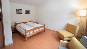 Een slaapkamer met een houten bed, een nachtkastje, een stoel en een vloerlamp.