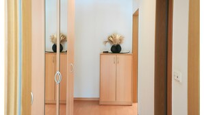 Een gang met een spiegelkast, een houten kastje met een vaas, en een deur die naar een andere kamer leidt.