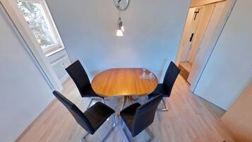Un comedor con una mesa redonda de madera, cuatro sillas negras, un reloj de pared y una lámpara colgante.