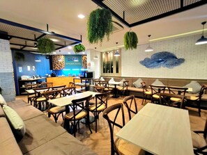 A restaurant with a blue counter, wooden tables and chairs, and a brick wall with a blue artwork. - Blue Neptuna Hotel Patong (Patong)
