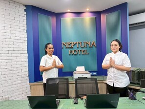 Un comptoir d’accueil avec deux employés, un mur bleu sur lequel est inscrit le nom de l’hôtel et un mur en briques.